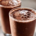 Two tall glasses filled with frothy, cold frozen hot chocolate, showing condensation droplets on the glass exterior.