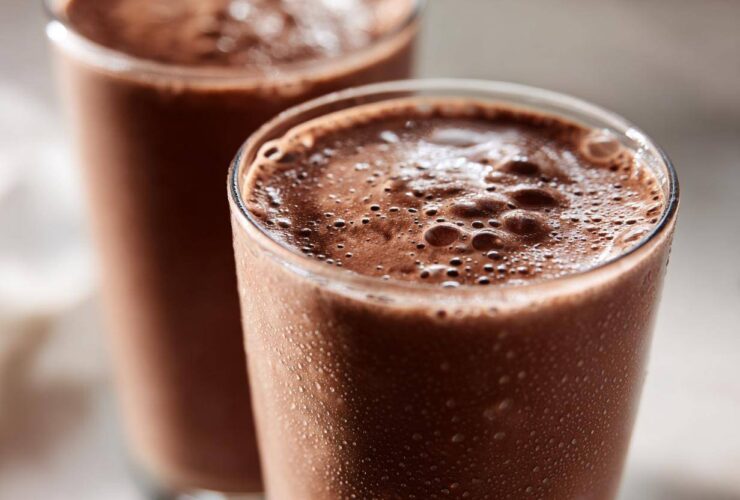 Two tall glasses filled with frothy, cold frozen hot chocolate, showing condensation droplets on the glass exterior.