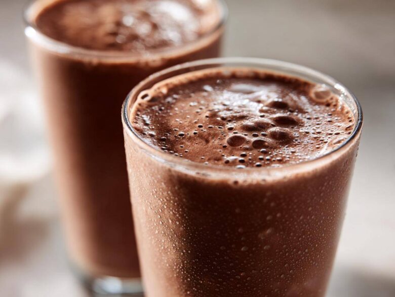 Two tall glasses filled with frothy, cold frozen hot chocolate, showing condensation droplets on the glass exterior.