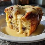A square slice of rich bread pudding studded with raisins, topped with thick vanilla sauce.
