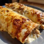 Two baked chicken enchiladas covered in melted, browned cheese, served on a gray plate.