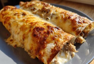 Two baked chicken enchiladas covered in melted, browned cheese, served on a gray plate.