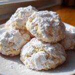 A stack of soft, crinkle-textured cool whip cookies heavily dusted with white powdered sugar on a white plate.