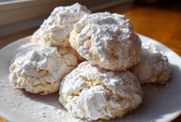 A stack of soft, crinkle-textured cool whip cookies heavily dusted with white powdered sugar on a white plate.