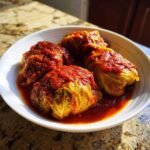 A white bowl filled with four savory Stuffed Cabbage Rolls smothered in rich, red tomato sauce.