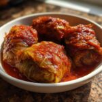 Four hearty Stuffed Cabbage Rolls swimming in a rich tomato sauce, served in a white bowl.