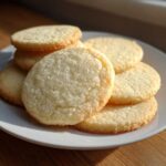 A stack of freshly baked, round sugar cookie treats piled on a white plate.