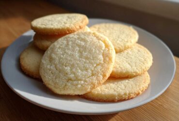 A stack of freshly baked, round sugar cookie treats piled on a white plate.