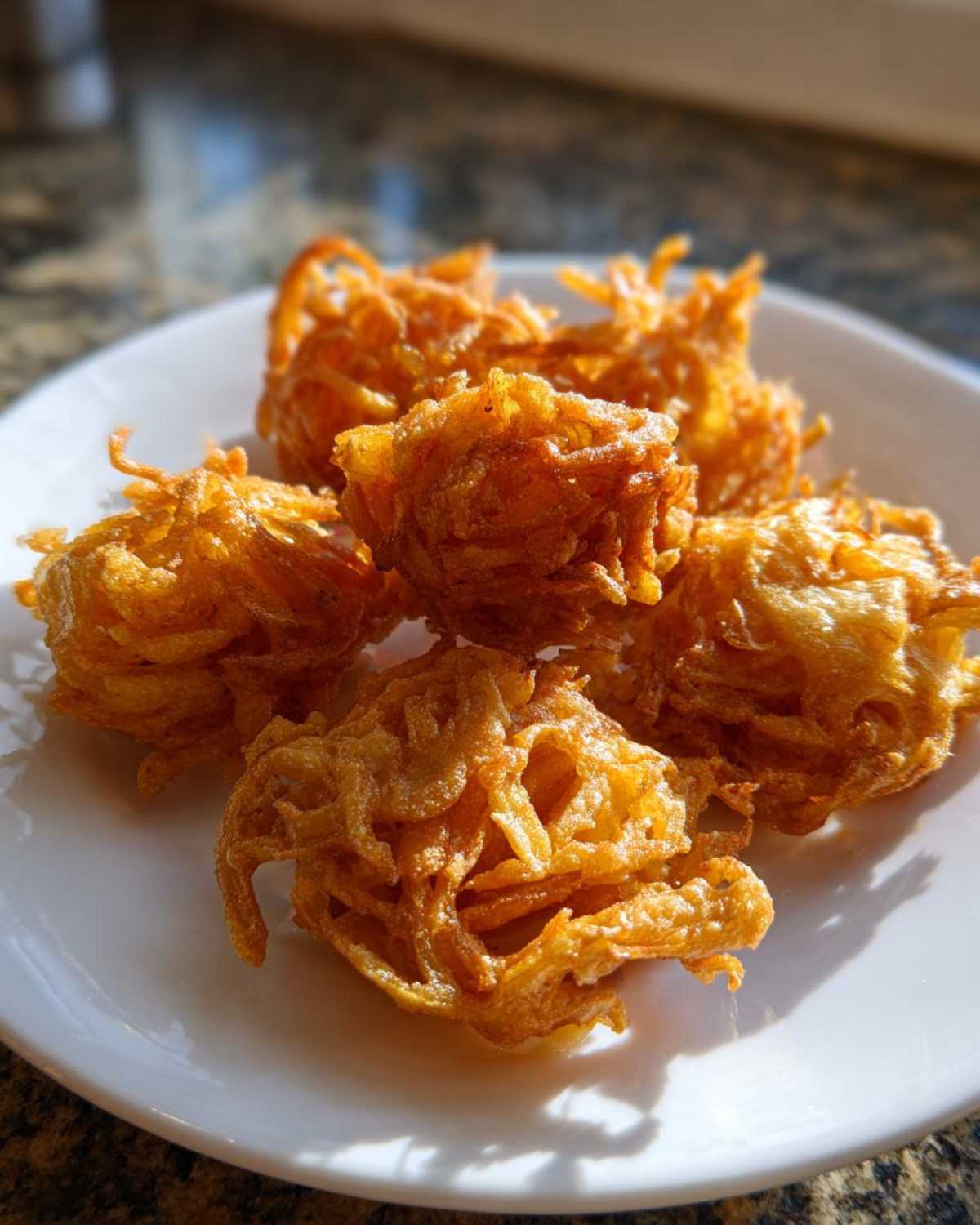A close-up of several crispy, golden brown Amish Onion Fritters piled on a white plate.