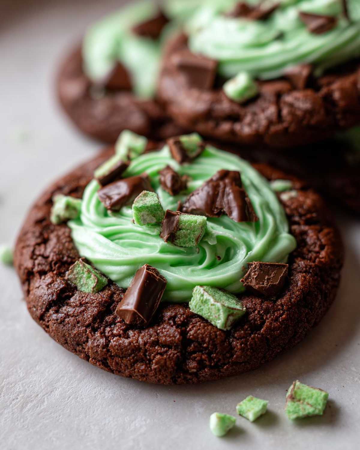 Close-up of a rich chocolate Andes Mint Cookies topped with bright green mint frosting and chopped Andes mint candies.