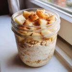 Close-up of apple cinnamon overnight oats in a glass jar, topped with diced apples and cinnamon.
