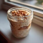 A glass jar filled with creamy apple cinnamon overnight oats, topped with a sprinkle of cinnamon.