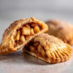 Close-up of apple pie cookies cut in half, showing chunky apple filling and cinnamon sugar coating.