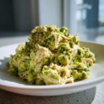A mound of creamy avocado chicken salad featuring shredded chicken mixed with mashed avocado and spices, served on a white plate.