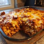 A close-up of baked chicken enchilada dip in a glass dish, showing shredded chicken filling and a bubbly, browned cheese topping.
