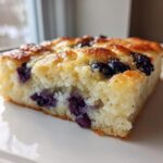 Close-up of a thick slice of blueberry sheet pan pancakes showing a fluffy interior and golden brown top.