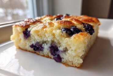 Close-up of a thick slice of blueberry sheet pan pancakes showing a fluffy interior and golden brown top.