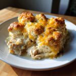 A close-up serving of creamy chicken cobbler topped with golden biscuits and melted cheddar cheese.