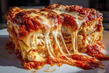 A gooey, cheesy slice of ravioli lasagna with melted mozzarella stretching over rich tomato sauce.