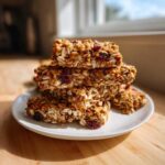 A stack of chewy homemade granola bars made with oats and dried cranberries, resting on a white plate.