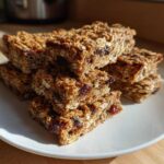 A stack of chewy homemade granola bars, rich with oats and dried cranberries, resting on a white plate.