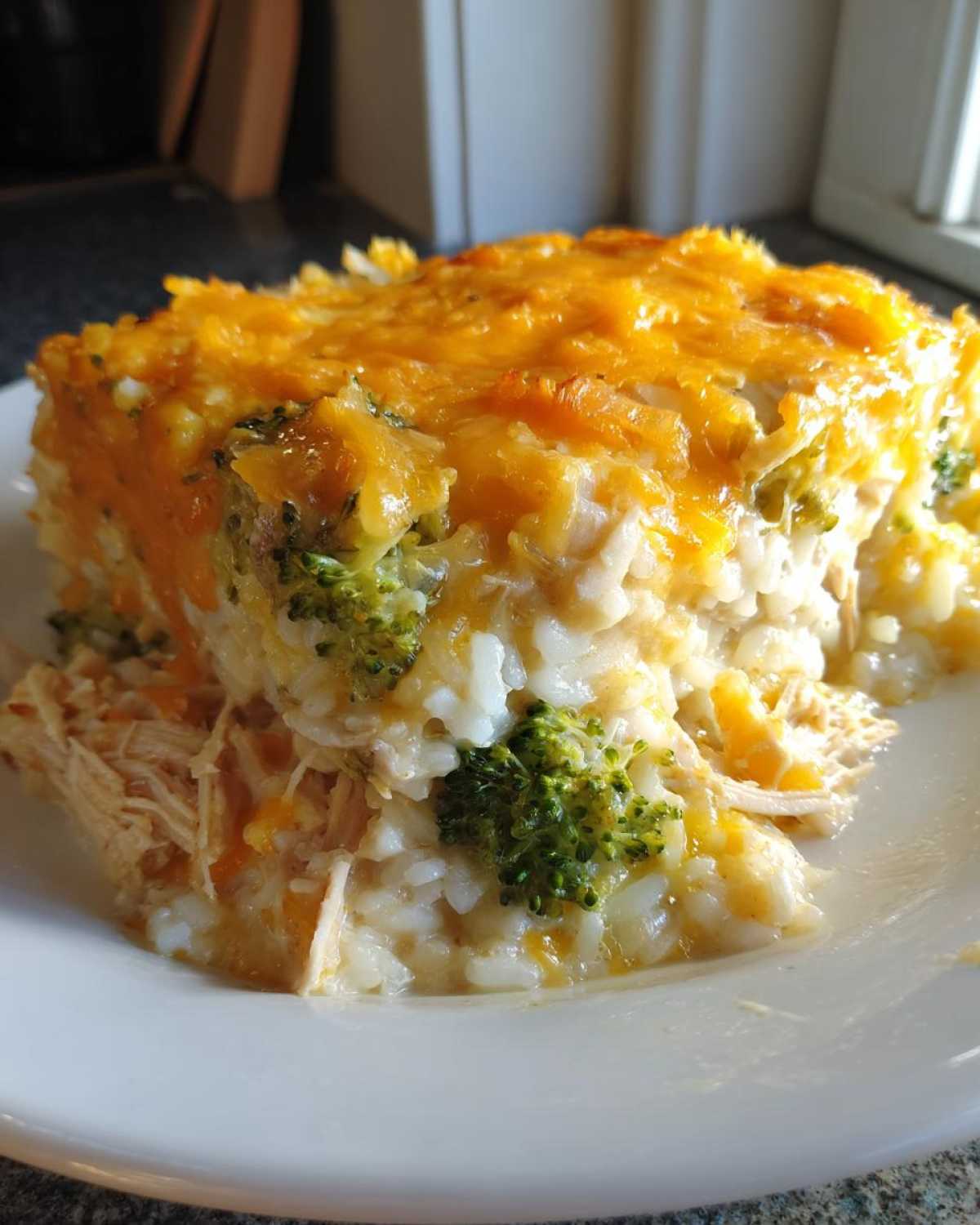 A close-up serving of creamy chicken broccoli rice casserole topped with melted cheddar cheese.