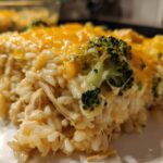 Close-up of a serving of creamy chicken broccoli rice casserole topped with melted cheddar cheese.