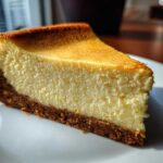 A close-up shot of a perfect, smooth slice of cheesecake showing the creamy filling and graham cracker crust.