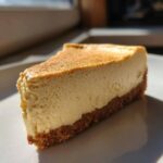 A close-up of a smooth, creamy slice of cheesecake recipe with a thick graham cracker crust.