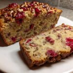 A loaf of cranberry walnut bread, sliced to show the interior packed with bright red cranberries and walnuts.
