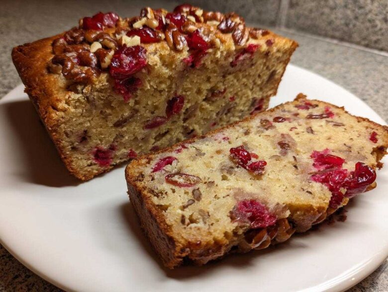 A loaf of cranberry walnut bread, sliced to show the interior packed with bright red cranberries and walnuts.