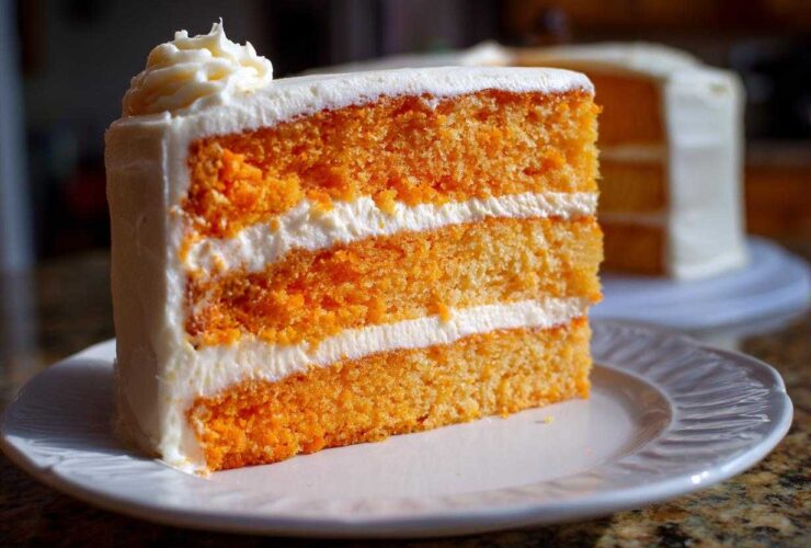 Close-up of a three-layer slice of bright orange Creamsicle Cake filled and frosted with white cream cheese icing.