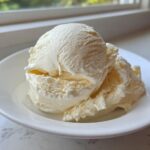 Three scoops of creamy, pale yellow banana ice cream served in a white bowl.
