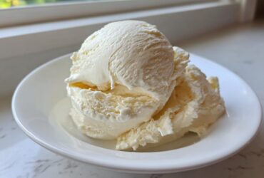 Three scoops of creamy, pale yellow banana ice cream served in a white bowl.