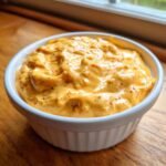 A close-up of thick, creamy, orange beer cheese dip speckled with spices, served in a white ramekin.