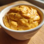 Close-up of rich, orange beer cheese dip topped with black pepper and chili flakes in a white bowl.
