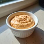 A close-up of creamy, orange-hued big mac sauce speckled with red pepper flakes in a small white ramekin.