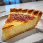 A close-up of a single slice of buttermilk pie showing its creamy yellow interior and deeply browned, caramelized top crust.