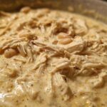 Close-up of creamy white chicken chili recipe featuring shredded chicken and white beans in a rich sauce.