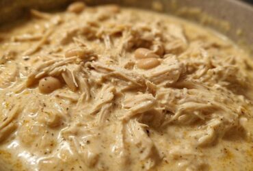 Close-up of creamy white chicken chili recipe featuring shredded chicken and white beans in a rich sauce.
