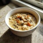 A close-up of a white bowl filled with creamy chicken and wild rice soup, featuring shredded chicken and orange carrots.