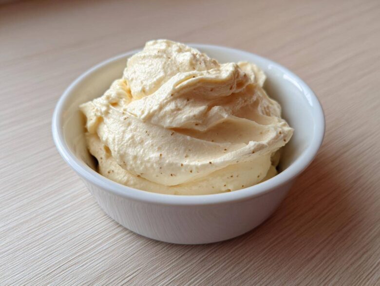 A close-up of rich, creamy garlic aioli, perfectly piped or spooned into a small white bowl.