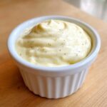 Close-up of thick, creamy garlic aioli, flecked with pepper, served in a small white fluted ramekin.