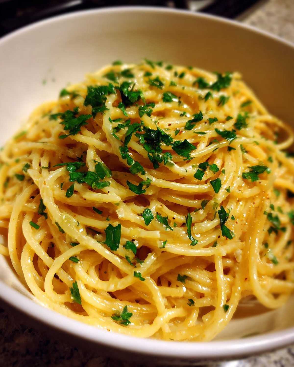 A close-up shot of a bowl filled with bright yellow Creamy Lemon Pasta, topped generously with fresh chopped parsley.