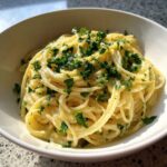 Close-up of a white bowl filled with delicious Creamy Lemon Pasta, topped generously with fresh chopped parsley.