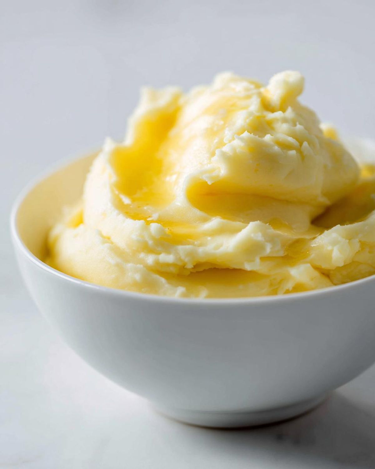 A close-up of fluffy, creamy mashed potatoes topped with a drizzle of melted butter in a white bowl.