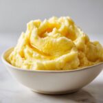 A close-up of fluffy, creamy mashed potatoes topped with a drizzle of melted butter in a white bowl.