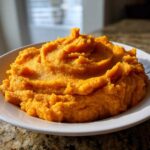 A generous serving of bright orange, creamy mashed sweet potatoes piled high on a white plate.