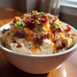 A white bowl filled with creamy Million Dollar Dip, topped generously with shredded cheddar and crispy bacon bits.