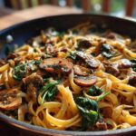 Close-up of creamy mushroom pasta with wilted spinach tossed in a skillet, featuring sliced, browned mushrooms.